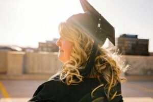Adult woman in black cap and gown looks into the sun.